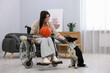 © New Africa - Woman in wheelchair with basketball ball and her service dog indoors