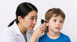 © kodidesign - Female pediatrician examining a young boy's ear with an otoscope. Professional medical checkup in a clinic. Asian doctor and child patient. Healthcare and wellness concept