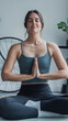 © Daniel - Young woman sits cross-legged with palms together, eyes closed, practicing seated meditation and gentle yoga at home to promote mindfulness, calm, breath awareness and physical well-being.