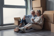 © Daniel - Older couple sits on the floor among cardboard boxes, using a laptop to organize moving details, discuss plans and enjoy a quiet moment while settling into their new home.