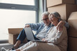 © Daniel - Elderly couple smiling while unpacking boxes and browsing a laptop together in new home