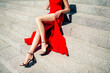 © deagreez - Elegant woman in red dress sitting on stone steps showing long legs and black high heels fashion portrait