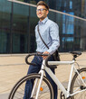 © muse studio - Smiling professional man in glasses walks a white bicycle outdoors near a modern glass office building during daytime