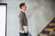 © Novak - Successful middle-aged businessman holding a laptop while walking up the stairs in a modern corporate building.
