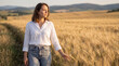 © ViskBx - Young woman walking through a golden wheat field at sunset, gently touching the crops with her hand