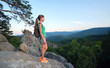 © bilanol - Sportive woman standing alone on hillside trail. Female hiker enjoying view of summer nature from rocky cliff on wilderness path. Active lifestyle concept