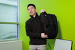 © fotolite - A young Asian male student slings a black backpack over his shoulder while smiling in a bright campus study room, ideal for back to school, student lifestyle, or campus life concepts.