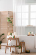 © Pixel-Shot - Interior of stylish bathroom with bathtub, folding screen, houseplants, burning candles and cosmetic products on stepladder