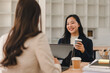 © PRIME STOCK LAB - Smiling Asian businesswoman holding coffee during a meeting with a colleague at a modern office desk