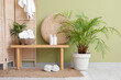© Pixel-Shot - Folding screen, houseplants and wicker basket with clean folded towels on bench near green wall