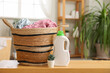 © Pixel-Shot - Wicker basket with laundry, houseplant and bottle of detergent on wooden table in room