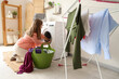 © Pixel-Shot - Young woman with laundry basket putting clothes into washing machine at home