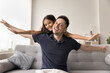 © fizkes - Lovely kid and father play together seated on sofa, outstretching their arms, like flying, smile, looking at camera, dreaming about family vacation, holidays, spend carefree leisure on weekend at home