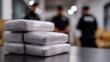 © Curioso.Photography - Stack of seized drug packages on table with blurred police officers in background, symbolizing crime investigation and law enforcement.