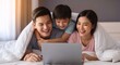 ©  Tsvyk L. - Young asian family having fun under a blanket in bed, watching a laptop, with their child hugging mother and father in a cozy home setting. High quality photo