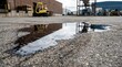 © Николай Чайка - Spill of dark oil on asphalt surface in an industrial area with a forklift and storage pallets visible in the background, showcasing a commercial setting
