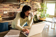 © Davor - Woman working on laptop with coffee in home kitchen