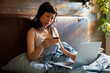 © Davor - Young woman shopping online with credit card in bed at home