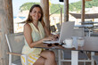 © SISMIZ - Woman working remotely on laptop at beach cafe
