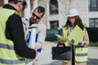 © qunica.com - Construction workers review building plans on a job site while wearing hard hats and hi vis vests. A team of engineers and architects examines documents and blueprints outdoors during inspection.