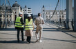© qunica.com - Construction workers wearing high-visibility vests and hard hats walk on a bridge during an inspection. The engineers conduct a site survey on an urban pedestrian bridge, discussing safety and plans.