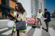 © qunica.com - A female construction engineer wearing a safety vest reviews plans on a tablet while holding a hard hat. Two colleagues discuss blueprints in the background at an urban construction site.