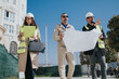 © qunica.com - Three construction professionals wearing hard hats review a large blueprint at an outdoor site. An engineer and colleagues inspect plans and discuss project details during a site visit.