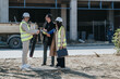 © qunica.com - Construction engineers review project plans and discuss progress while wearing hard hats and safety vests. The team consults blueprints and talks on-site at an active building construction area.