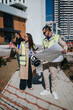 © qunica.com - Male and female construction professionals wearing high-visibility vests examine blueprints and discuss project details.