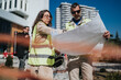 © qunica.com - A female engineer and a male architect examine large blueprints while wearing high-visibility vests. They review building plans together on an urban construction site.