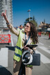 © qunica.com - A female engineer in a high-visibility vest points and directs work while holding a helmet and tablet.