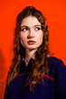 © deagreez - Young woman portrait against a bright orange background with thoughtful expression, curly hair and casual navy sweater — fashion and beauty studio headshot