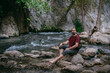 © Anna - A young male tourist near a clear mountain stream in the rocks overgrown with greenery, on a summer day