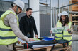 © qunica.com - Construction engineers in hard hats and high-visibility vests review blueprints and maps at a building site. A small team discusses plans and site layout beside fencing and construction materials.