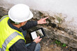 © Arttali_Neuro - Inspector in white helmet and reflective vest examining damaged building foundation with tablet, structural damage assessment, construction site inspection, property risk evaluation.