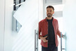 © Prostock-studio - A man walks through a glass door into an office. He has short hair and a beard. He looks happy and holds a tablet. Bright light fills the room.