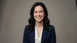 © Vectscape - Middle aged businesswoman with dark wavy hair wearing navy blue jacket and white top smiling warmly for professional studio headshot on gray background representing corporate identity and excellence.