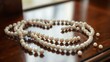 © wenqing - unanimity. Delicate pearl necklace with undone clasp on a polished wooden surface. lifestyle magazines, social media lookbooks, designed for lifestyle magazines and social media content.