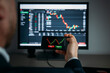 © erika8213 - Close up of trader hand holding smartphone, using trading app with stock market charts for financial analysis and monitoring investment data.