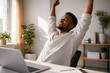 © Frendev - A man stretches with raised arms near his laptop, illustrating office movement, energy reset, and burnout prevention during focused work