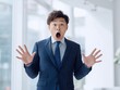 © Jumpei - 驚きの表情で口を大きく開けて目を見開く紺色のスーツを着た若いビジネスマンの男性