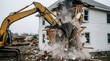 © Tahmina Kazim - Yellow excavator demolishing old white house with dust and debris.