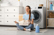 © Pixel-Shot - Beautiful young happy woman with basket of clean laundry and detergent meditating at home
