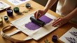 © Dollar - Close up of a person using a printing brayer to apply purple ink onto a leaf-patterned tote bag
