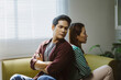 © Crystal - Young couple sitting back to back on a sofa at home, experiencing relationship problems, conflict, and disagreement