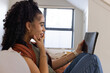 © wavebreak3 - Woman sitting on light-colored sofa in living room holding tablet, wearing green top and bracelets