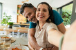 © Wavebreak Media - Diverse couple posing closely in bright home dining area, reaching toward smartphone, taking selfie