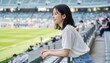 © AiPhoto - スタジアムの最前列の手すりにもたれてサッカー観戦する女性
