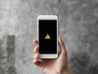 © Jumpei - 警告アイコンが表示されたスマートフォンを片手で持つ人物とコンクリート壁の背景素材