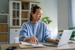 © Miljan Živković - Asian woman working remotely with laptop and notebook at home